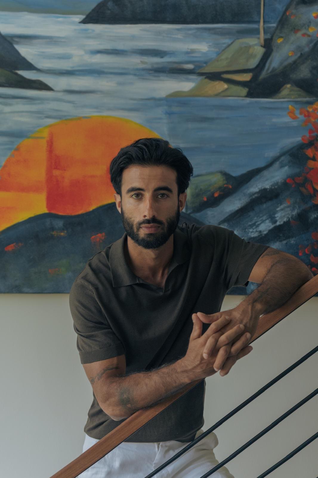 Suroesh Jazayeri leaning on a stair rail in front of a painting.